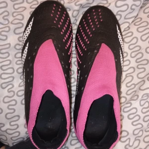 Adidas Predator fotbollsskor i svart och rosa - Säljer ett par Adidas Predator fotbollsskor i svart och rosa. Skorna har en cool design med rosa detaljer och en strumpliknande passform för extra komfort. De har dobbar som ger bra grepp på planen. Perfekta för fotbollsträning eller match! Använt men gott skick. Köptes höst 2023, inte mkt använda. Säljes pga slutat fotboll.Nypris ca 1600. Mitt pris 800kr pris kan diskuteras och sänkas vid snabb affär. Finns I billingsfors, Dalsland. Kan frakta men det står för Köparen.