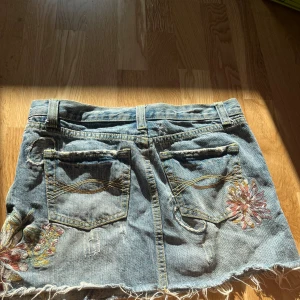 Lågmidjad jeanskjol från abercrombie and fitch - Lågmidjad kort jeanskjol från abercrombie and fitch, med super söta broderings detaljer💗💗 pris kan diskuteras vid snabb affär, skriv vid frågor!