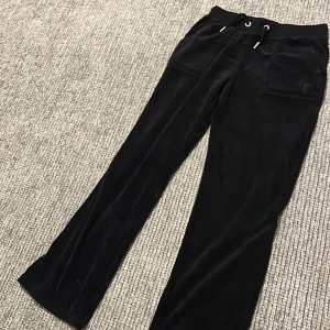 Svarta mjukisbyxor från Juicy Couture - Säljer ett par svarta mjukisbyxor från Juicy Couture. De är superbekväma och har en snygg design med fickor bak och dragsko i midjan. Perfekta för en avslappnad dag hemma eller en snabb tur på stan.