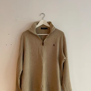 Beige tröja från Ralph Lauren - Säljer en snygg beige tröja från Ralph Lauren. Den har en dragkedja framtill och är långärmad, perfekt för både höst och vår. Tröjan är i bomull och har en klassisk stil med en liten broderad logga på bröstet. Passar perfekt för en casual look!