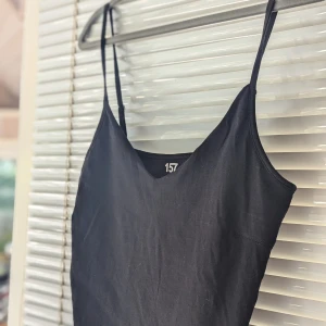 Svart linne från 157 - Svart linne från 157 i storlek XL. Den är ärmlös med smala axelband och har en enkel, elegant design. Materialet är 95% bomull och 5% elastan, vilket gör den både bekväm och stretchig.små i storleken