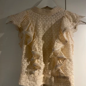 Croppad blus i spets - Croppad blus i spets med hög krage och öppen rygg med knyte baktill. Går att ha utan BH då volangen täcker brösten. 