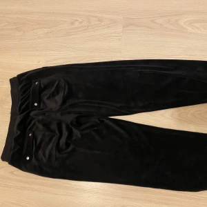 Svarta mjukisbyxor från Juicy Couture - Säljer ett par svarta mjukisbyxor från Juicy Couture. De är supermjuka och bekväma, perfekta för en chill dag hemma eller en avslappnad utflykt. Byxorna har en dragsko i midjan för justerbar passform och fickor fram. De är i bra skick och redo för en ny ägare!