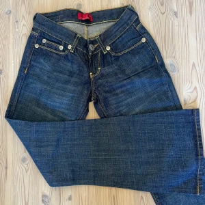 Lågmidjade bootcut jeans - Lågmidjade bootcut/utsvängda blå jeans med bruna sömmar. Märket är Cross Jeans och storleken 25x30 (W25 L30). Mycket fint skick! 