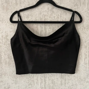 Svart satinlinne - Säljer ett snyggt svart satinlinne med smala axelband som är justerbara. Perfekt för en utekväll eller fest! Det är croppat och har en stilren design som passar till det mesta.