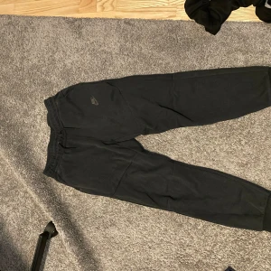 Svarta mjukisbyxor från Nike - Säljer ett par svarta Nike tech mjukisbyxor, bra skick och storlek är Xl barn passar 158-170, hör av er för mer bilder.