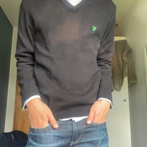 Svart tröja från Lyle & Scott - Säljer en svart tröja i storlek S från Lyle & Scott med en snygg v-ringning. Tröjan har ett grönt märke på bröstet och är perfekt för hösten. Den har ett ytterst litet hål vid armen som inte syns när den är på. Skriv för frågor!🤙