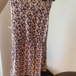 Blommig klänning - Säljer en superfin blommig klänning med massor av färger som rosa, lila och vit. Perfekt för sommardagar eller en mysig vårpicknick. Klänningen har en normal passform och är i ett mjukt och bekvämt material.