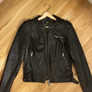 Svart skinnjacka från FB Sister - Säljer en snygg svart skinnjacka från FB Sister(Newyorker) i storlek S. Jackan har en cool bikerstil med dragkedjor och quiltade detaljer på axlarna. Den har en dragkedja framtill och flera fickor med dragkedjor. Perfekt för höst och vår! den är i bra skick och har lite slitage eftersom den har använts, men inget märkvärdigt. 
