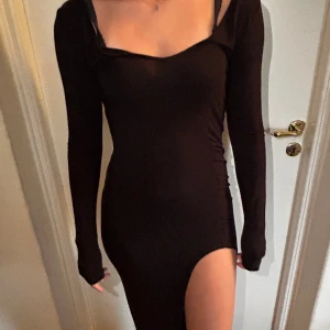 Svart långklänning med slits - Säljer en elegant svart långklänning med en djärv slits på sidan. Klänningen har långa ärmar och en tunn ocg tight passform som framhäver figuren.