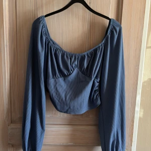 Blå långärmad topp - Säljer en superfin blå topp med långa ärmar och en lätt croppad design. Toppen har en snygg rynkad detalj vid halsringningen och är perfekt för både vardag och fest. Materialet känns mjukt och bekvämt.