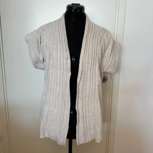 Beige stickad kofta från Zara Knit - Säljer en supermysig beige stickad kofta från Zara Knit. Den är gjord av en blandning av bomull, viskos, nylon och angora, vilket gör den både mjuk och varm. Koftan har korta ärmar och en öppen design, perfekt för lager-på-lager under hösten. Den är använd men i bra skick och redo för en ny ägare!