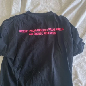 Svart t-shirt från Palm Angels - Säljer en svart t-shirt från Palm Angels med en cool rosa palm på framsidan och text på baksidan. T-shirten är kortärmad och perfekt för en avslappnad stil. Den är i bomull och känns riktigt skön att ha på sig. Passar perfekt till både vardag och fest! 🎉 Nypris 1200 vårt pris 449.