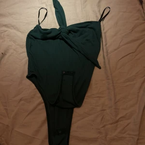 Grön ribbad bodysuit från Shein - Säljer en snygg grön ribbad bodysuit från Shein. Den har smala axelband och en knytning framtill som ger en cool look. Perfekt för en utekväll eller fest! Bodysuiten är i storlek M och har knäppning i grenen för enkel på- och avtagning.