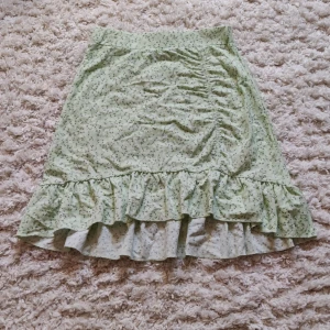 Grön volangkjol med vita blommor - Säljer denna fina kjolen som är lite mer grön i verkligheten än på bilderna. Den är i bra skick förutom att lappen är avklippt eftersom den syndes lite igenom 💗