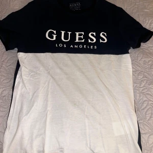 Svart och vit t-shirt från Guess - Säljer en snygg svart och vit t-shirt från Guess med texten 'Guess Los Angeles' tryckt på bröstet. T-shirten är kortärmad och har en klassisk passform. Perfekt för en avslappnad stil!