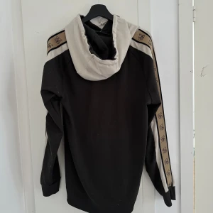 Sikslik hoodie - Denna sikslik hoodien är som en kram i tygform - bekväm och stilren. Med svart-beige vibes är den perfekt för alla tillfällen. 