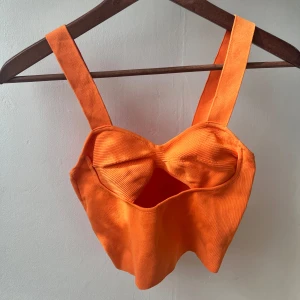 Orange ribbad korsettopp - Säljer en superfin orange korsettopp med breda axelband. Toppen är ribbad och har en snygg passform som framhäver figuren. Perfekt för sommarens fester eller en dag på stan!