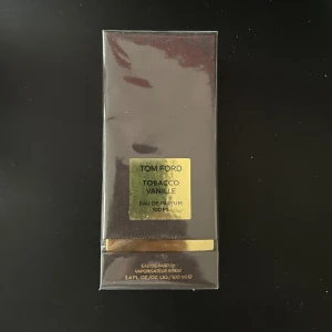 Tom Ford Tobacco Vanille Eau de Parfum - Säljer en lyxig parfym från Tom Ford, Tobacco Vanille, i en elegant mörkbrun förpackning med guldiga detaljer. Flaskan innehåller 100 ml av denna ikoniska doft som kombinerar rika noter av tobak och vanilj. Perfekt för den som vill ha en sofistikerad och varm doft.