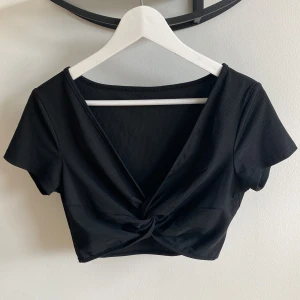Kort topp med knytdetalj - Svart, kort topp med knytdetalj och ribbat tyg. 95% polyester och 5% elastan. Aldrig använd. 