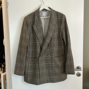 Rutig kavaj från H&M - Säljer en snygg rutig kavaj från H&M i storlek M. Kavajen har en klassisk design med dubbelknäppning och långa ärmar. Perfekt för både vardag och fest!