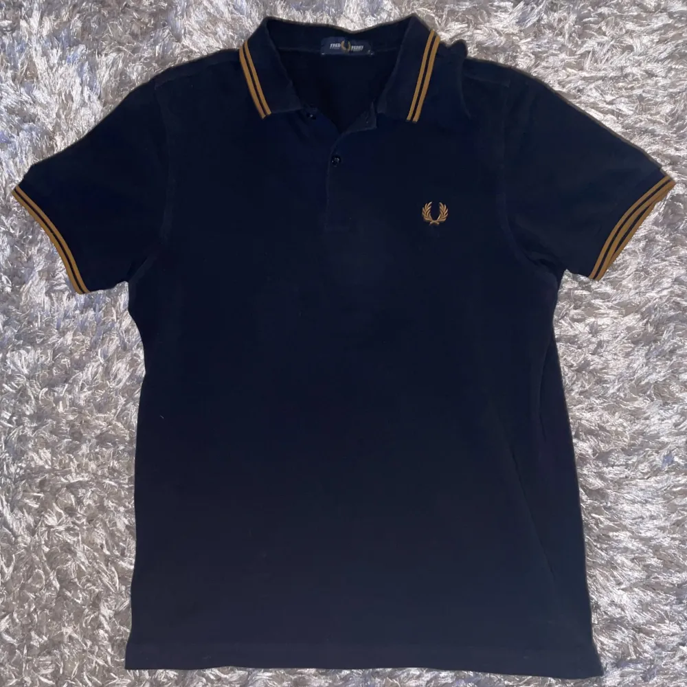 Riktigt snygg Fred Perry piké i marinblå färg med bruna streck. Sparsamt använd, utan deffekter. Tröjan är i storlek M. Kan gå ner i pris vid snabbaffär.. T-shirts.