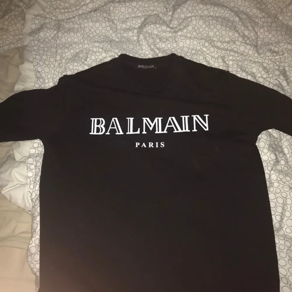 Säljer en snygg svart tröja från Balmain med deras ikoniska logga i vitt på framsidan. Tröjan har långa ärmar och är perfekt för en stilren look. Passar både till vardags och fest!. Neuletakit & Villapaidat.