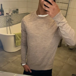 Beige tröja från Jack & Jones - Säljer en stilren beige tröja från Jack & Jones i superfin merinoull. Tröjan har en klassisk rund hals och långa ärmar, perfekt för en elegant och bekväm look. Passar bra till både jeans och chinos.