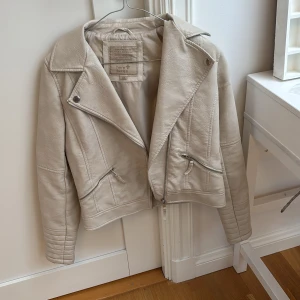 Beige/ vit skinnjacka - Snygg vit skinnjacka med dragkedja och stiliga detaljer. Jackan har en klassisk bikerstil med snedställd dragkedja och två fickor med dragkedja. Säljer på grund av att den inte kommer till användning längre men den är i fint skick med inga skador som jag vet om. Jackan är köpt second hand tidigare. Skriv för fler frågor!