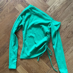 Grön ribbad offshoulder-topp - Snygg grön ribbad offshoulder-topp med lång ärm och knytning i sidan. Passar både vardag och fest!