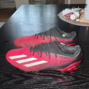 Rosa fotbollsskor från Adidas - Säljer ett par rösa fotbollsskor från Adidas med svarta och vita detaljer. Skorna har snörning och en modern design med tre vita ränder på sidan. Perfekta för fotbollsplanen med en slitstark sula. Modell adidas speedportal .1 alltså högsta modellen. Storlek 42
