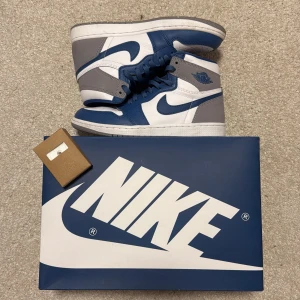 Air Jordan 1 retro high OG storlek 42/UK 7,5 - Snygga Nike Air Jordans i en stilren kombination av blått, vitt och grått inga tecken på bärning bortsätt från den lite smutsiga sulan, men det går enkelt att tvätta bort. Skorna har klassisk snörning och en perforerad tå för extra ventilation. Perfekta för dig som vill ha en ikonisk stil med komfort.