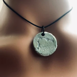 Made By prisförslag- Halsband Lera stjärntecken berlock - Inte som på bilden - Stjärnorna är samma, formen olika och konstruktionen hur leran lägger sig skiljer sig åt. Därför är det ett Unikt halsband med en rund berlock som har ett stjärntecknet ingraverat. Berlocken hänger i ett enkelt svart band, vilket ger en stilren och minimalistisk look. Perfekt för den som vill bära sitt stjärntecken nära hjärtat. 