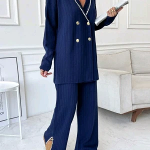 Mörkblå ribbad kostym - Elegant mörkblå ribbad kostym med dubbelknäppt kavaj och guldknappar. Kavajen har en v-ringad design med vita detaljer längs kanten. Byxorna är vida och matchar kavajen perfekt. Perfekt för en stilren look.