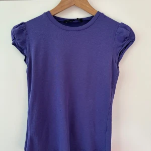 Lila topp från French Connection - Säljer en snygg lila topp från French Connection med korta puffärmar. Toppen är tillverkad i ett mjukt material och har en rund halsringning. Perfekt för en stilren look.