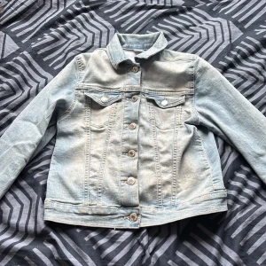 Ljusblå jeansjacka från &Denim - Säljer en snygg ljusblå jeansjacka från &Denim. Jackan har klassisk design med knappar framtill och två bröstfickor. Perfekt för en avslappnad stil. Passar storlek 146.