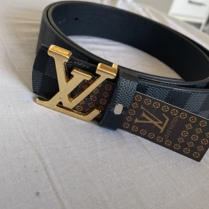 Svart rutigt bälte med gullig logga - Jag säljer ett svart bälte med rutor som har en guldig logga. Bältet passar till olika stilar och är in nytt skick, har bara prövats på. Pris kan diskuteras vid snabb affär