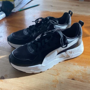 Svarta och vita sneakers från Puma - Snygga svarta och vita sneakers från Puma med en sportig design. Skorna har en bekväm passform med snörning och en tjock vit sula. Oanvända i nyskick! (Pris kan diskuteras)