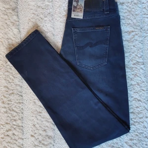 Blå jeans Thin Finn - Snygga blå jeans från Nudie Jeans, modell Thin Finn. De har en slim passform och är tillverkade i denim med en klassisk femficksdesign. Jeansen har en snygg tvätt med lätt slitna detaljer som ger en cool look. Helt nya & oanvända. 