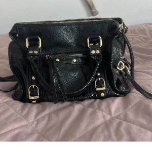 Svart glittrig handväska - Snygg svart handväska med glittrig yta och guldfärgade detaljer. Den är i bra skick och inköpt för 800 kr och knappt använd💕obs inte mina bilder, men skriv för fler 