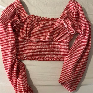 Rutig off shoulder topp - Säljer en söt röd- och vitrutad offshoulder-top med långa ärmar och volangdetaljer. Toppen är croppad och smockad 🥰
