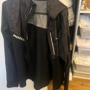 Svart vindjacka från Newline - Säljer en svart vindjacka från Newline med dragkedja och reflekterande detaljer. Jackan har långa ärmar och en hög krage. Perfekt för löpning eller andra utomhusaktiviteter. 🏃‍♂️