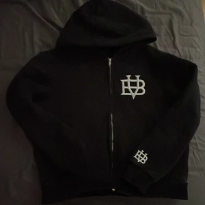 Svart hoodie från Bvaldi - Säljer en svart hoodie från Bvaldi med dragkedja och broderad logga på bröstet och ärmen. Perfekt för en stilren look med en skön passform.  Tröjan är aldrig använd ändast tvättad en gång. Säljer därför att den var för liten. Ny pris är 1200kr