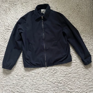 Mörkblå jacka från H&M - Säljer en stilren mörkblå jacka från H&M med dragkedja framtill. Jackan har långa ärmar och elastiska muddar vid ärmslut och nederkant. Perfekt för en casual look.