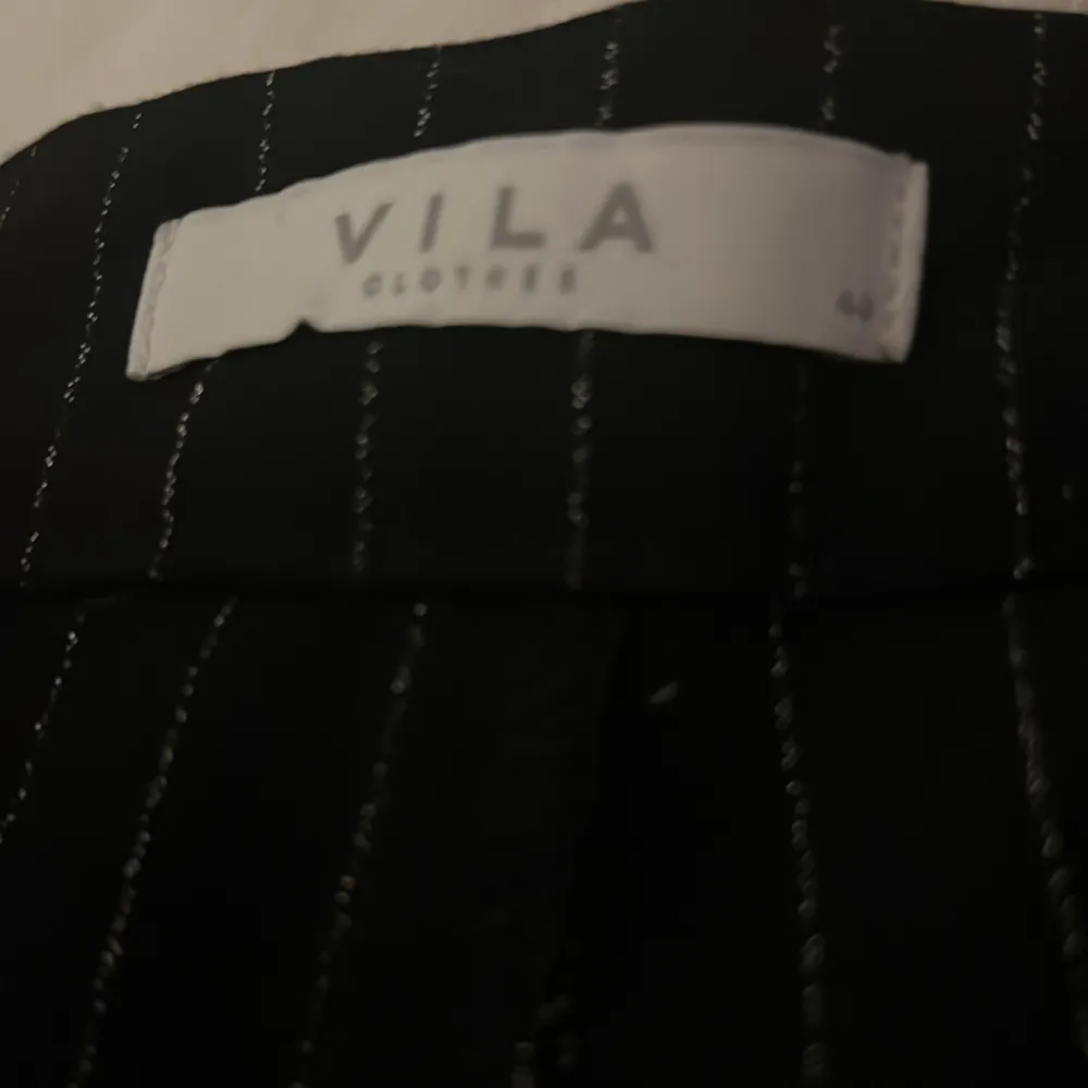 Snygga svarta byxor från Vila med vita ränder. Byxorna har en elegant design och är perfekta för en stilren look. De är tillverkade i ett bekvämt material och har en elastisk midja för extra komfort. Hör av dig vid intresse (aldrig använt). Farkut & Housut.