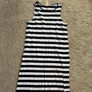 Randig klänning från H&M - Säljer en stilren randig klänning från H&M i svart och vit. Klänningen är ärmlös och har en avslappnad passform, perfekt för en somrig dag. Den är gjord i ett mjukt och bekvämt material.