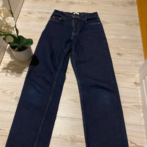 Blå jeans från Grunt - Säljer ett par klassiska blå jeans från Grunt i modellen 90s Raw Blue. De har en rak passform med fem fickor och en snygg mörkblå färg. Perfekta för en avslappnad stil.                  