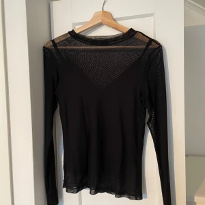 Svart mesh topp från Rut&Circle - Snygg svart mesh topp från Rut&Circle i storlek S. Toppen har långa ärmar och en transparent design som ger en trendig look. Perfekt för lager-på-lager styling eller som statement-plagg.