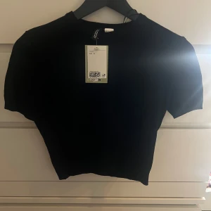 Svart kortärmad topp från H&M - Snygg fin stickad svart topp från H&M med korta ärmar. Köpt men aldrig använd. Den är ganska kort i magen och har etiketten kvar. 