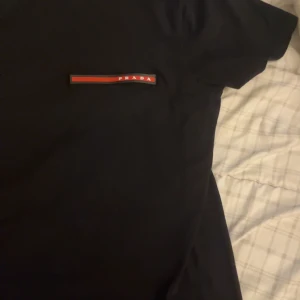 Svart t-shirt  - Snygg svart t-shirt med en diskret logga i rött och vitt på bröstet. Perfekt för en stilren look. T-shirten har en klassisk passform och är kortärmad.